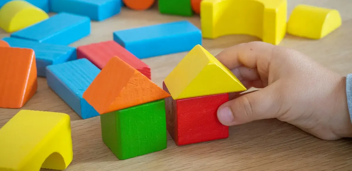 Eine Hand spielt mit bunten Holzbausteinen.