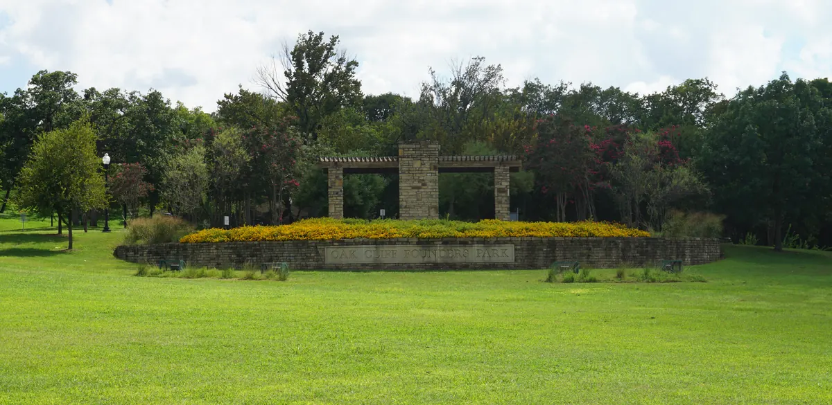 Oak Cliff Founders Park entrance with its stone name plaque and flower beds in Dallas.